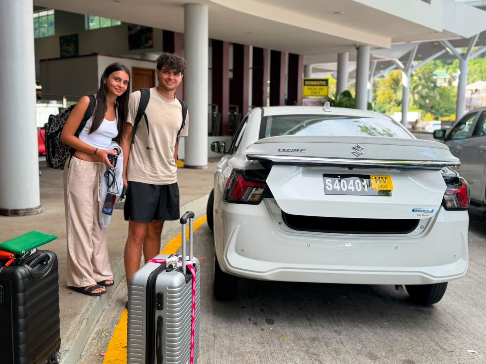 A group of visitors posing beside a white Suzuki